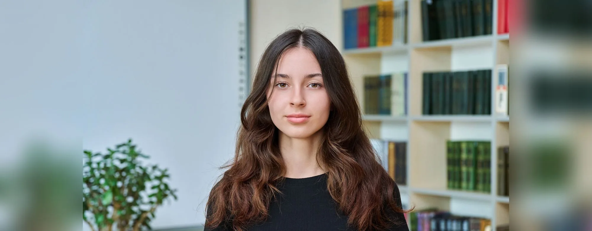 A student standing in a bright library, looking at the camera