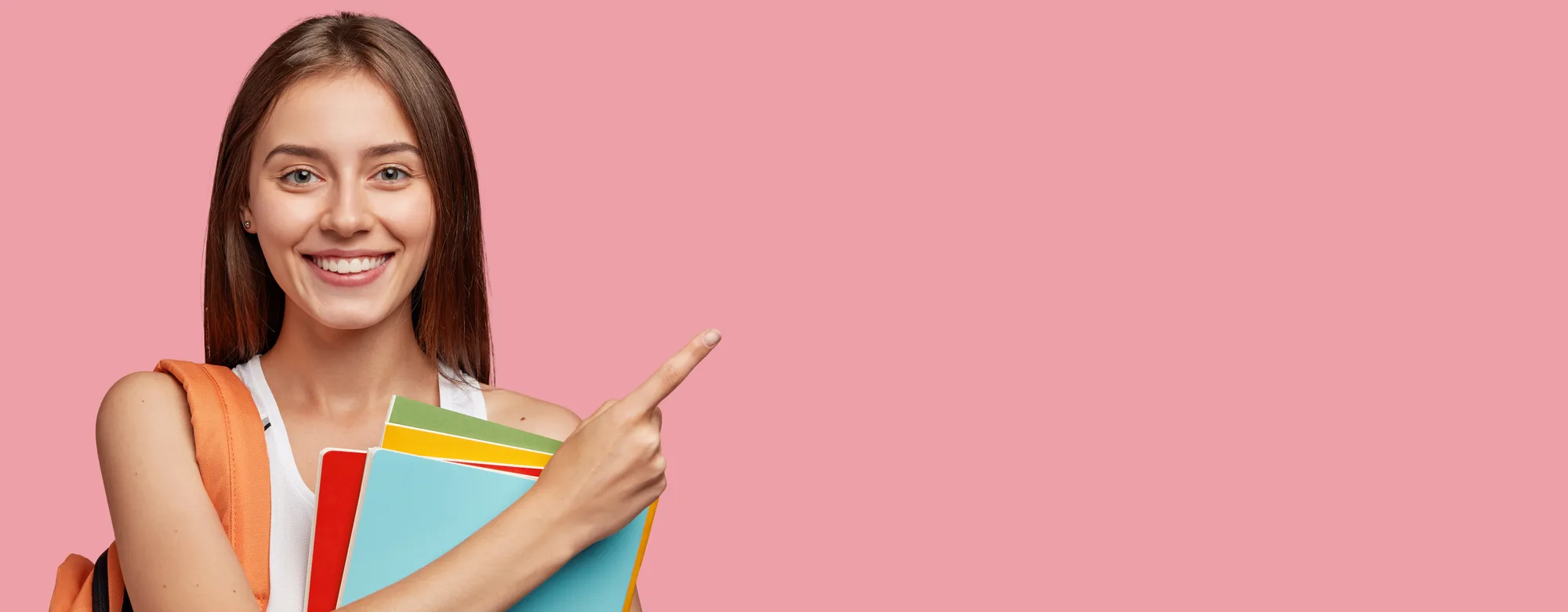 A smiling student holding notebooks and pointing to the side