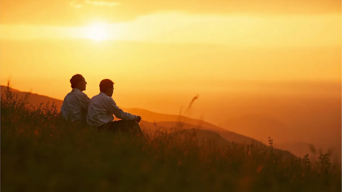 Two friends reminisce on a grassy hill at dusk, illustrating “the year 2010” in Chinese: 二〇一〇年 (èr líng yī líng nián)