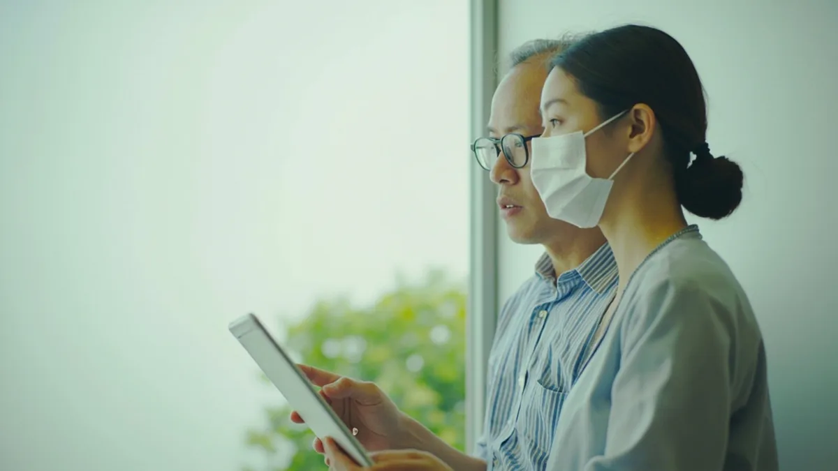 Two colleagues discuss a schedule while looking at a blank calendar, illustrating “has the time been set” in Chinese: 时间定了吗？ (shíjiān dìng le ma?)