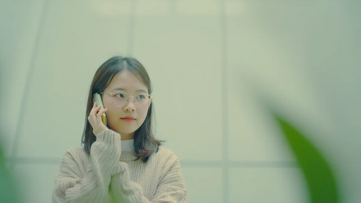 A young adult holds a smartphone to their ear in a quiet setting, illustrating “hello on the phone” in Chinese: 喂 (wéi)