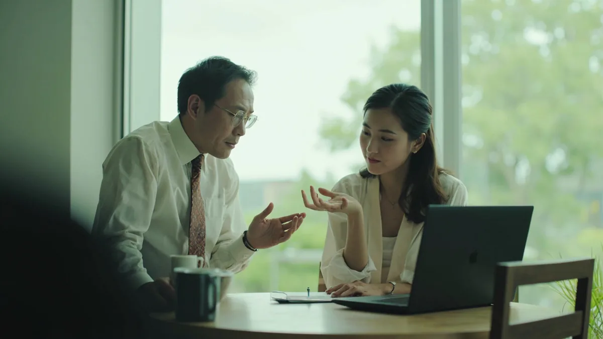 A person politely approaches a busy colleague, asking if they have a moment, illustrating “is now a good time” in Chinese: 您现在方便吗？ (nín xiànzài fāngbiàn ma?)